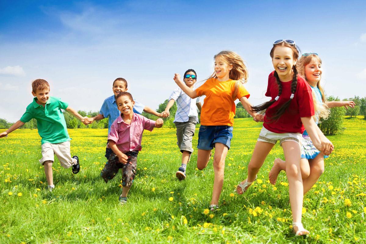 Sette bambini che corrono su un prato fiorito.