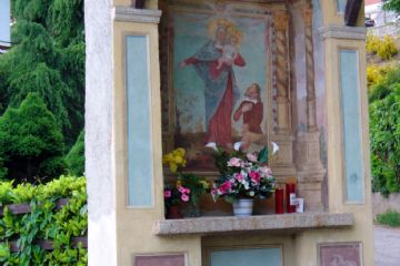 Cappelletta con frontale dipinto di azzurro e raffigurazione della Madonna con Bambino e uomo in ginocchio.