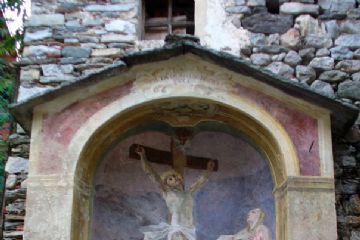 Cappelletta votiva con tetto in pietra raffigurante Gesù in croce e ai piedi di essa la Madonna e Maria Maddalena. Esterno affrescato in rosso scuro.