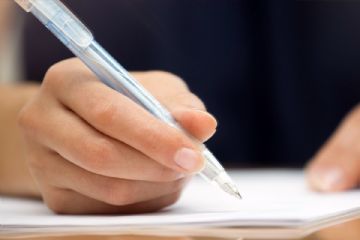 Una mano che scrive con una penna a sfera su un foglio bianco.