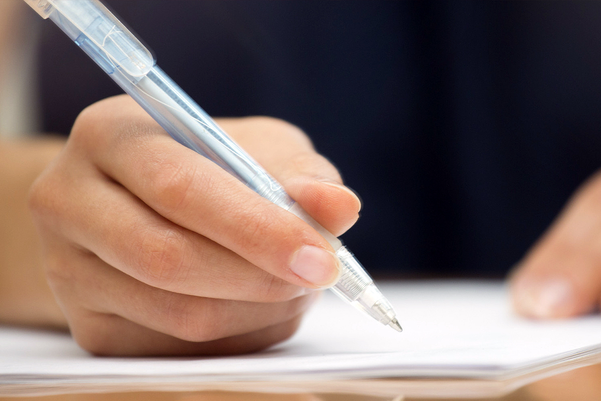 Una mano che scrive con una penna a sfera su un foglio bianco.