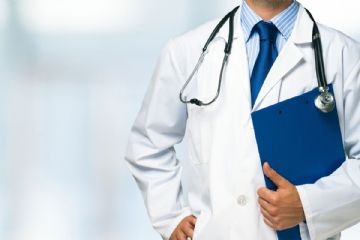Un medico in camice bianco con uno stetoscopio attorno al collo ed una cartella blu in mano.
