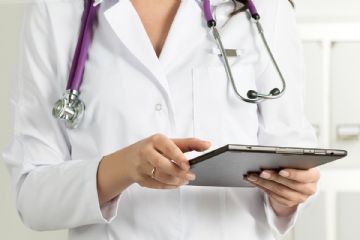 Busto di una dottoressa in camice bianco con stetoscopio intorno al collo e tablet in mano.