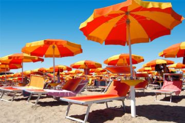 Una spiaggia con lettini ed ombrelloni aperti a spicchi gialli e rossi.