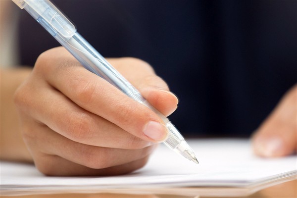 Una mano destra che impugna una penna biro per firmare un documento.