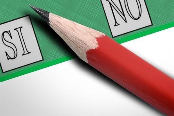 Una matita rossa posata su una scheda di votazione verde tra le caselle Sì e No.