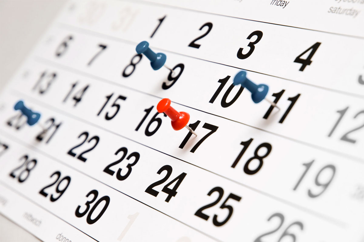 Un calendario mensile con alcuni giorni segnati da 3 spilli blu ed uno spillo rosso.